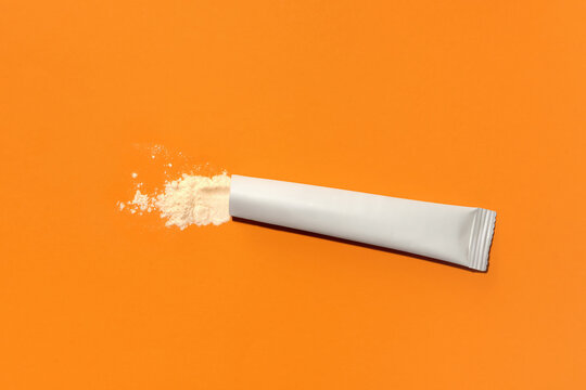 Sachet with collagen and vitamins in powder form on orange background.