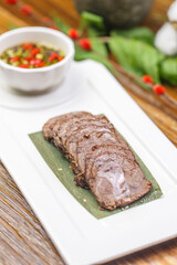 Beef tenderloin with dipping sauce on a rectangular white porcelain plate