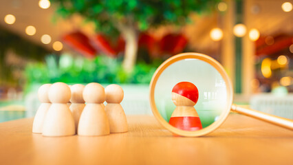 A magnifying glass and a red wooden figures with blur business man who search for someone who ‘s special person. Concept of Human resources management and recruitment.