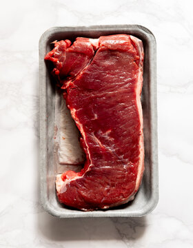 Raw beef steak in plastic tray on white marble