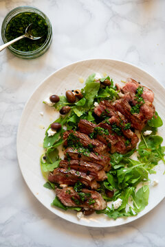 Sliced grilled steak with chimichurri and arugula salad
