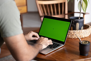 Unrecognizable man teleworking at home with green screen laptop