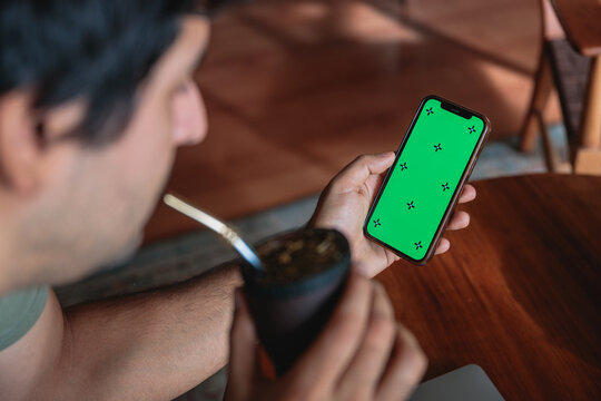 Latin man using smartphone with green screen and drinking yerba mate