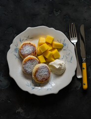 Delicious breakfast, brunch - homemade syrniki with sour cream and fresh mango on a dark...
