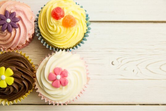 Naklejki Four frosted cupcakes are sitting on wood plank, fondant flowers, gumdrops, flat design, copy space