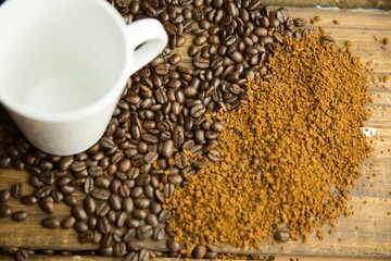 Showing flat top-down coffee beans blending into grounds mound on wood table with white ceramic mug © vectorfusionart