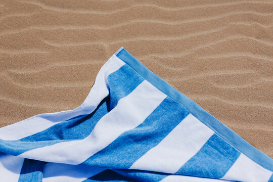 Blue and white striped beach towel lying on the sand on a sunny day