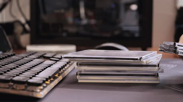 Close up of hands stacking CD cases near retro keyboard on desk in home office or media archive.