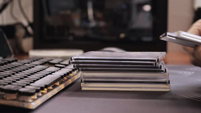 Hands sorting CD cases beside a vintage keyboard on desk, organizing physical media in retro workspace setting.