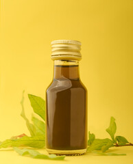 close-up of golden color herbal oil glass bottle with green herb leaves scattered, isolated yellow...