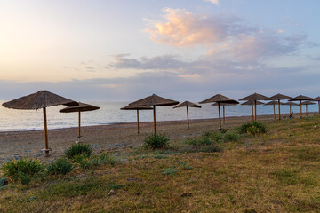 Straw beach umbrellas standing on seashore under sunset sky. Coastal scene with calm sea, ideal for...