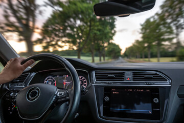 Driver view of car interior. Hand on steering wheel. Speed and motion.