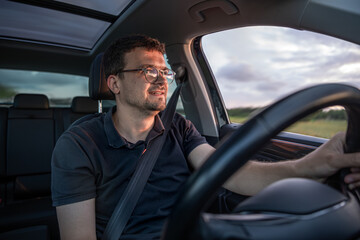Smiling driver. Sunset light inside car. Calm road motion
