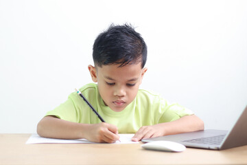 Young boy studying and doing homework at home with notebook and laptop. Concept of distance learning, education, homeschooling, and online classes for children.