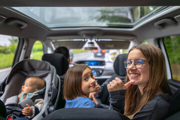 Smiling girl in car. Family trip moment. Baby in backseat.