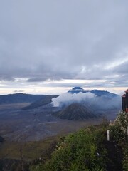The view of Mount Bromo releasing thick smoke, surrounded by a sea of sand and other mountains...