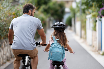 Close up, Father biking with his daughter to school in the morning through the neighborhood, healthy routine and affectionate parent-child relationship