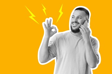 Handsome young man talking by phone and showing OK gesture on orange background