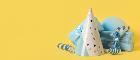 Party hat, gifts and decorations on yellow background with space for text