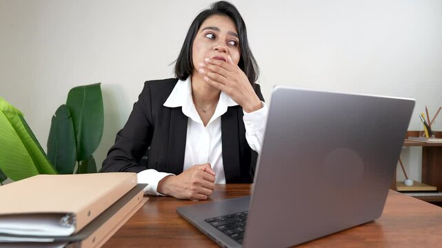 Close-up of tired working young millennial Indian businesswoman sits on chair at workplace desk looking at laptop screen yawning need sleep feels fatigue exhausted unwell.