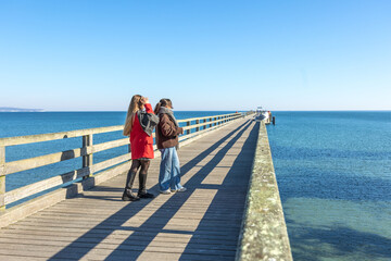 Two women on the pier. Rear view of two women walking along the pier. Sea.