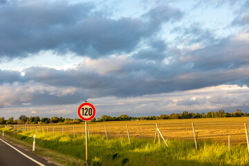 Speed limit sign 120. Sunset over field. Dramatic clouds