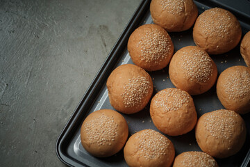 top view shot of a part of oven tray full with sesame burger buns put on rusty kitchen table with...