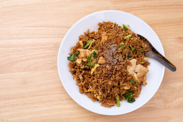 Thai style dark brown soy sauce fried rice with chicken, kale, and egg in white dish with short spoon on light wooden table