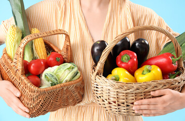 Young female farmer with wicker baskets full of different ripe vegetables on blue background,...