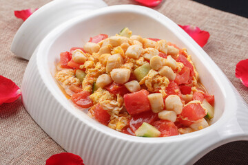 Stir-fried chicken with tomato and egg in a white shaped porcelain plate