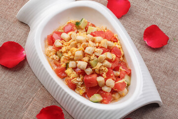 Stir-fried chicken with tomato and egg in a white shaped porcelain plate