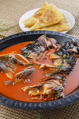 Black iron plate with thick soup and fish head in pancake