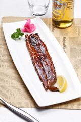 Japanese grilled eel in a rectangular porcelain plate on English wrapping paper