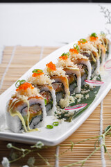 A long porcelain plate of crab roe professor rolls placed on a sushi curtain