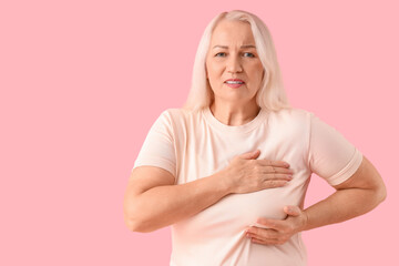 Mature woman suffering from breast pain on pink background. Cancer awareness concept