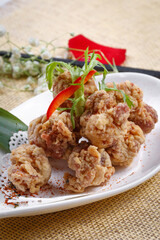 Fried chicken nuggets in a gooseneck porcelain plate are placed on a straw mat