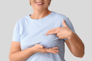 Mature woman checking her breast on light background, closeup. Cancer awareness concept