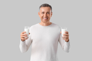 Mature man with glasses of milk on light background