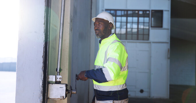 Mature man, garage door and open for shipping, stock or storage at warehouse for supply chain. African person, engineer and maintenance for gate, check or commercial distribution at industrial plant - Powered by Adobe