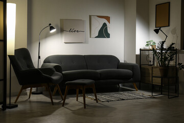Grey sofa, armchair and stool in interior of living room at night