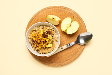 Wooden board with tasty oatmeal and apple on beige background