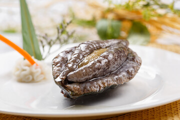 Fresh abalone in a round porcelain plate placed on a straw mat