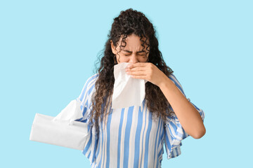 Young African-American woman with tissue suffering from allergy on blue background