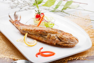 Japanese style grilled yellow croaker in a square porcelain plate placed on a straw mat