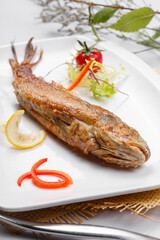 Japanese style grilled yellow croaker in a square porcelain plate placed on a straw mat