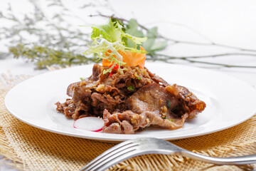 Round white porcelain plate of sizzling beef tongue with garlic sauce placed on a straw mat