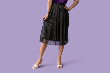 Legs of beautiful young woman wearing black long corrugated skirt on lilac background