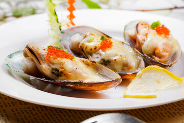 Baked mussels with mozzarella cheese in a round porcelain plate on English wrapping paper