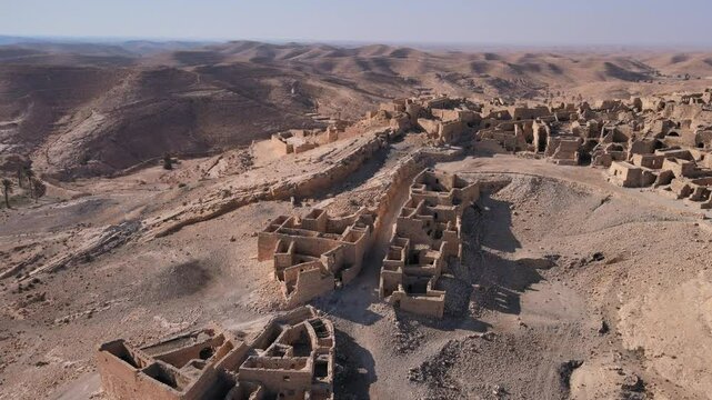An ancient village or town with a dry and dusty landscape, surrounded by rock walls, cliff sides, and dirt. Location: Tunisia, Gabes , Zraoua.