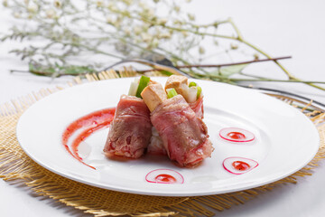 French foie gras beef rolls on a white round plate placed on a straw mat